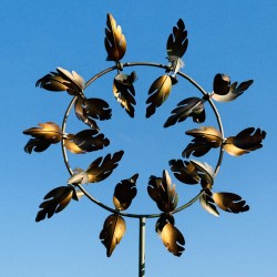 Decoratieve tuinwindmolen van gepatineerd metaal – elegantie en beweging voor uw buitenruimte gezien tegen een blauwe lucht